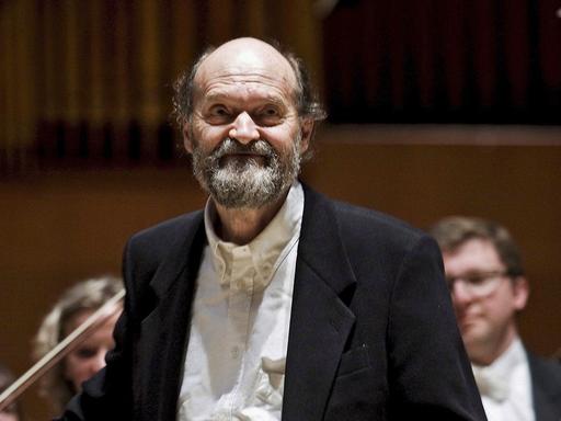 Der estnische Komponist Arvo Pärt im Jahr 2008, im Hintegrund die Musiker eines Sinfonie-Orchesters.