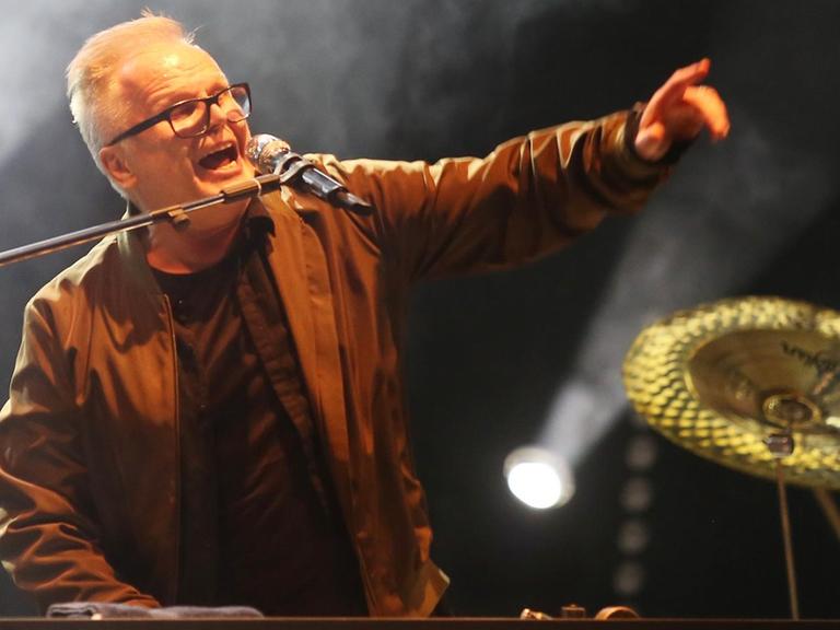 Herbert Grönemeyer singt auf der Bühne des Musikfestivals "Jamel rockt den Förster" in ein Mikrofon und hebt dabei den linken Arm.