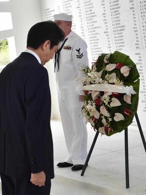 US-Präsident Obama und Japans Ministerpräsident Abe haben in der offizoiellen Gedenkstätte in Pearl Harbor auf je einem Ständer Kränze abgelegt. Im Hintergrund sind auf einer weißen Marmorwand die Namen der Gefallenen eingraviert.
