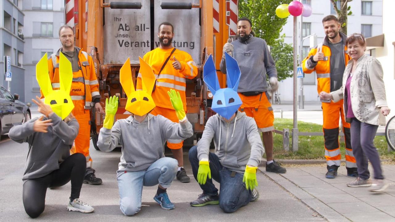 Drei Personen mit Hasenmasken, hinter ihnen stehen die Männer von der Müllabfuhr.