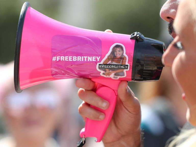 Zwei Menschen sprechen in ein rosa Megaphon, auf dem "Free Britney" steht.
