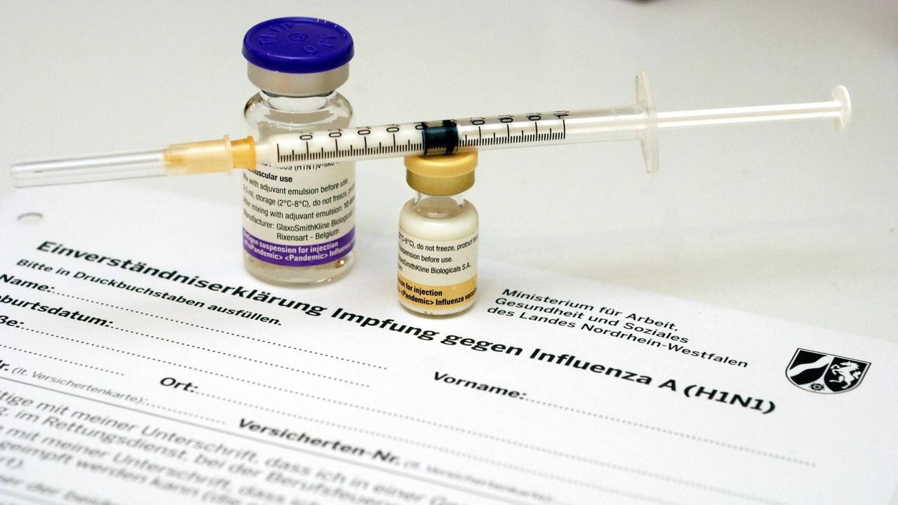 Glasdöschen mit dem Impfstoff Pandemrix und Impfspritze stehen auf einem Formular mit einer Impf-Einverständniserklärung 