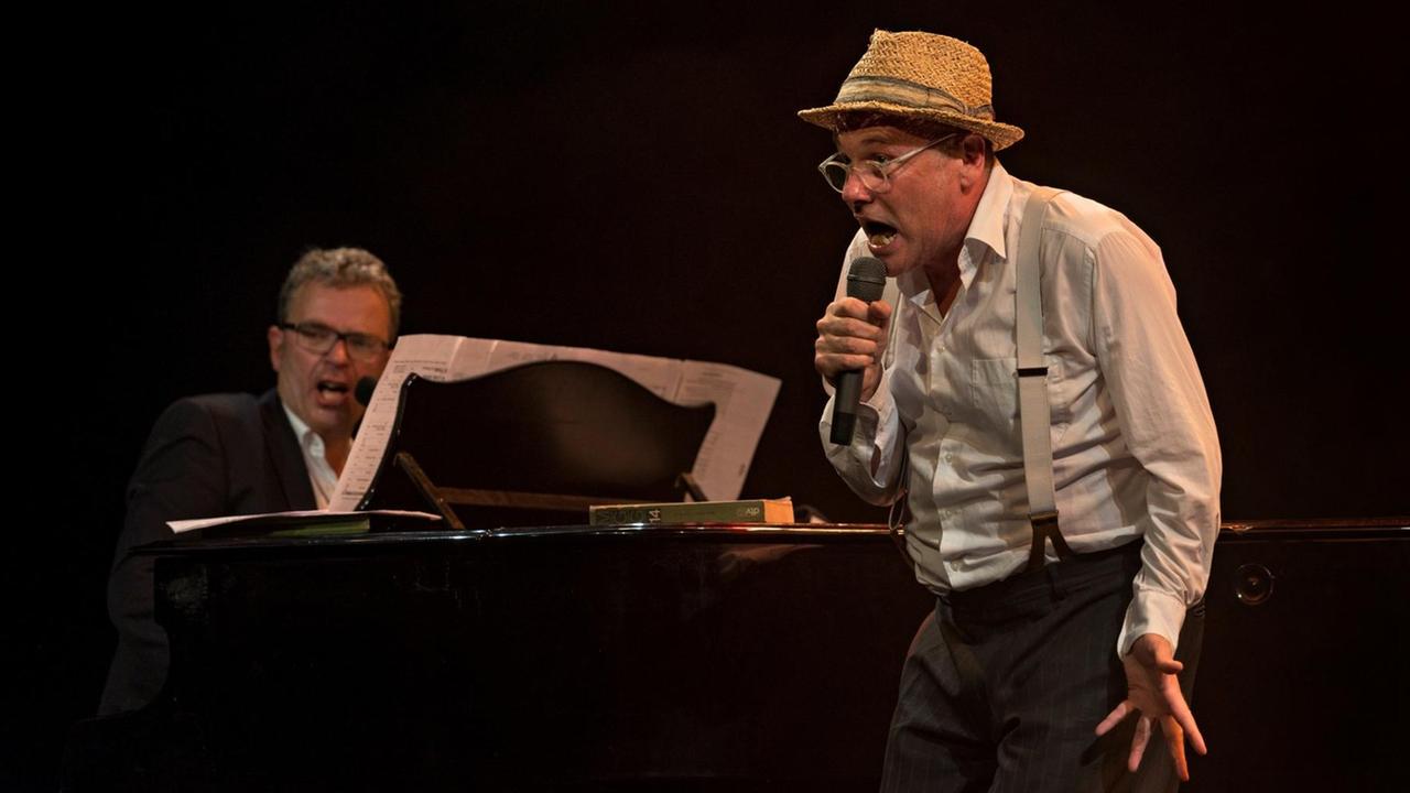 Das Künstlerduo Pigor und Eichhorn auf der Bühne. Hinten links am Klavier Benedikt Eichhorn, im Vordergrund Thomas Pigor am Mikrofon.