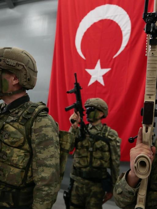 Türkische Soldaten mit Gewehren posieren vor einer Türkeiflagge