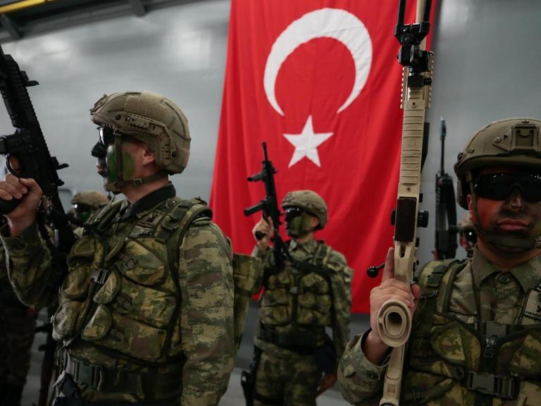 Türkische Soldaten mit Gewehren posieren vor einer Türkeiflagge