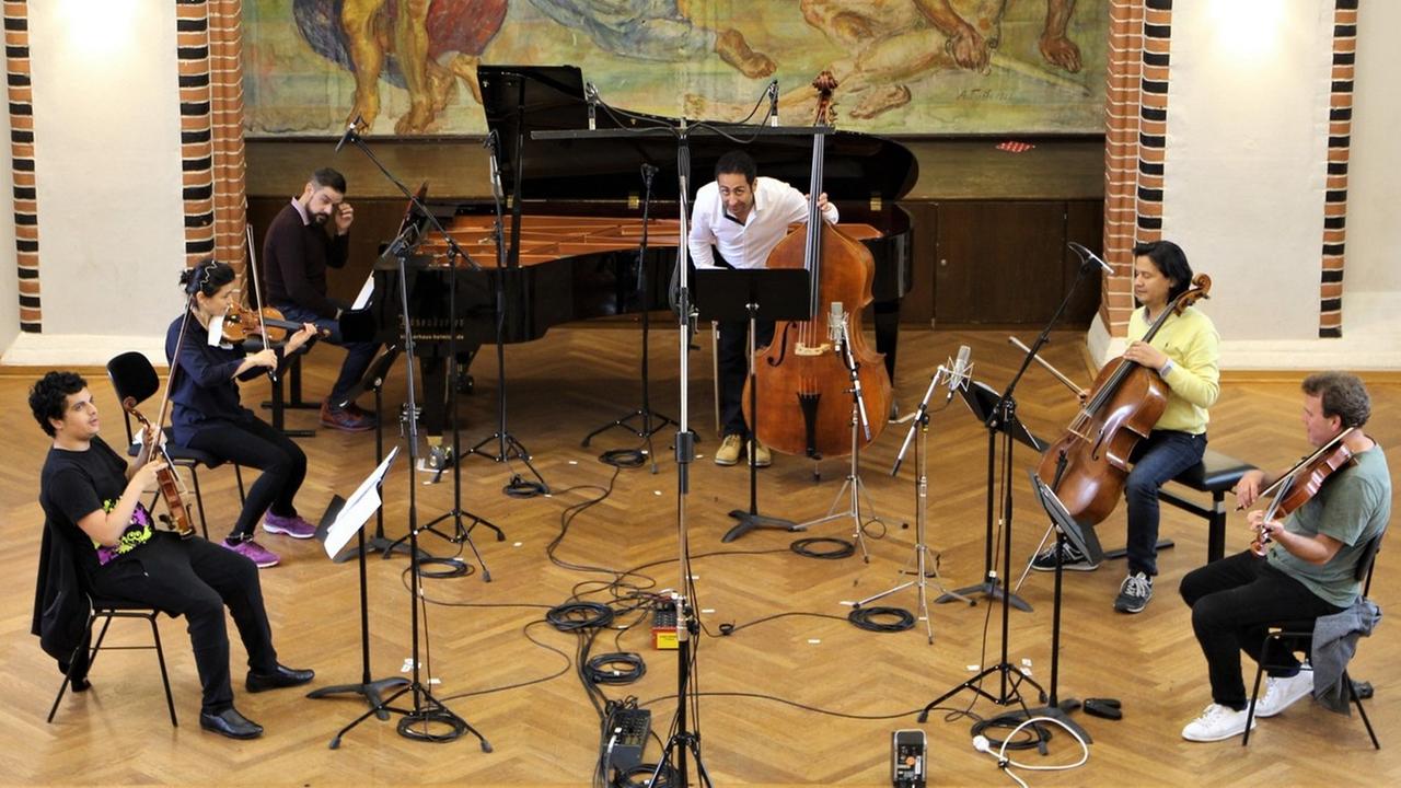 Sechs Musiker sitzen zwischen Mikrophonen und spielen.