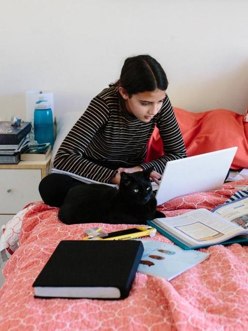 Eine Schülerin sitzt auf ihrem Bett und arbeitet. Homeschooling in Zeiten von Corona. (Symbolbild)
