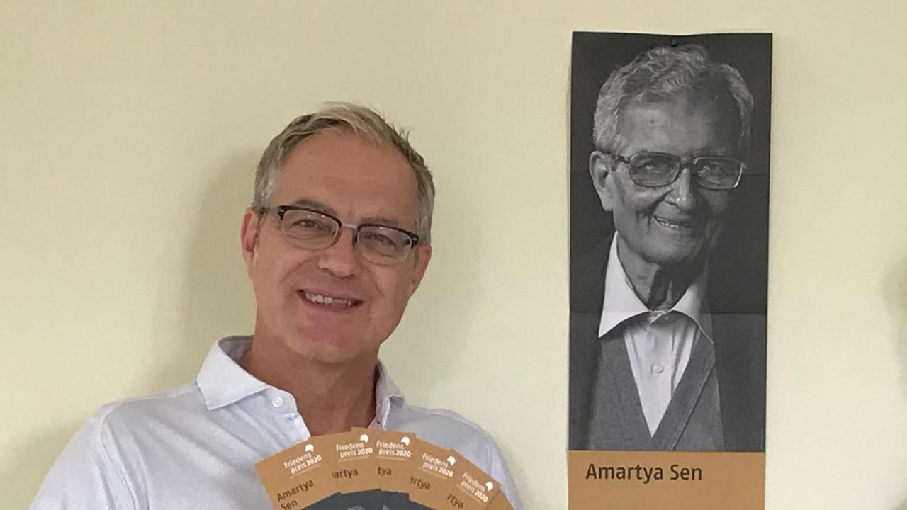 Martin Schult vom Börsenverein des Deutschen Buchhandels e.V. posiert neben einem Plakat von Amartya Sen, dem diesjährigen Preisträger des Friedenpreises des Deutschen Buchhandels (2020)