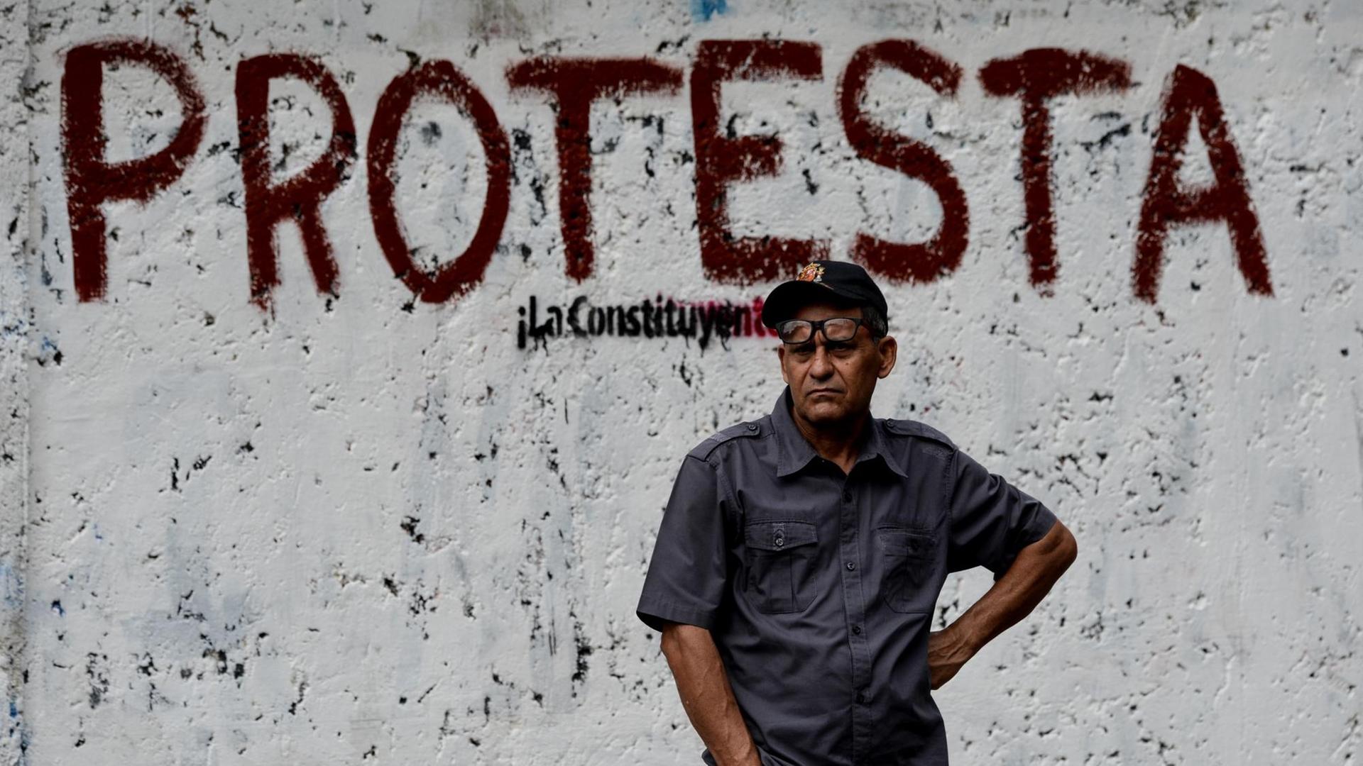 Ein Mann steht in Caracas vor einem Protest-Graffiiti.