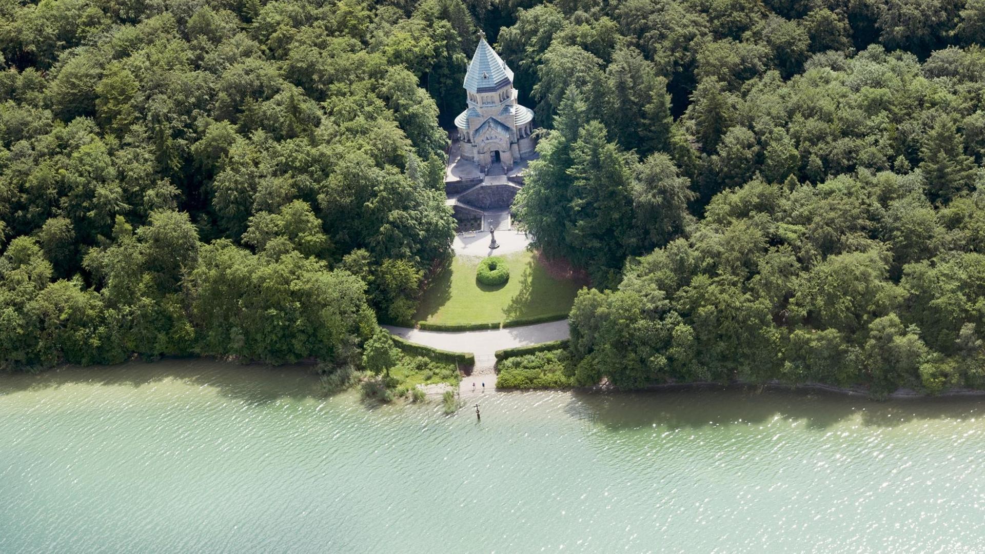 Ein Holzkreuz steht im Wasser des Starnberger Sees (Oberbayern) vor der Votivkapelle, die in einem Wäldchen am Ufer steht. Vor 125 Jahren ertrank hier König Ludwig II. von Bayern, der in unmittelbarer Nähe zur Kapelle gefunden wurde.