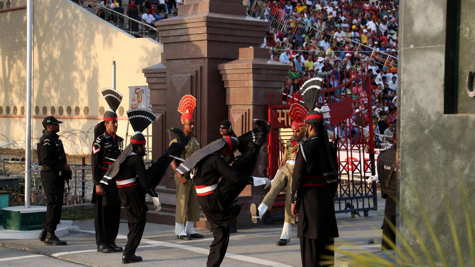 Pakistanische Soldaten in schwarzen Uniformen treffen auf indische Soldaten während einer Fahnenzeremonie am einzigen Grenzübergang in Wagah. Viele Zuschauer aus den verfeindeten Staaten verfolgen die "Beating retreat ceremony".