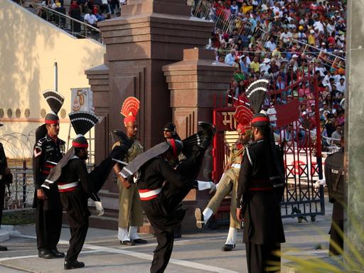 Pakistanische Soldaten in schwarzen Uniformen treffen auf indische Soldaten während einer Fahnenzeremonie am einzigen Grenzübergang in Wagah. Viele Zuschauer aus den verfeindeten Staaten verfolgen die "Beating retreat ceremony".
