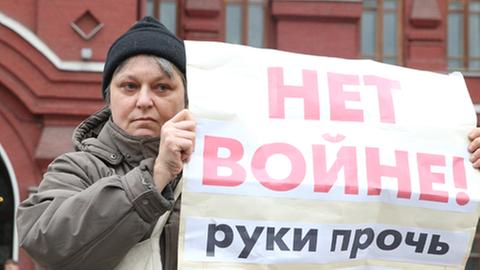 Demonstrantin hält auf dem Moskauer Roten Platz ein Plakat in die Fotokamera.