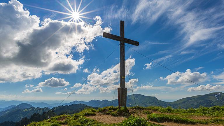 Gipfelkreuz auf einem Berg in Bayern, dahinter reissen die Wolken auf. Gipfelkreuz auf einem Berg in Bayern, dahinter reissen die Wolken auf.