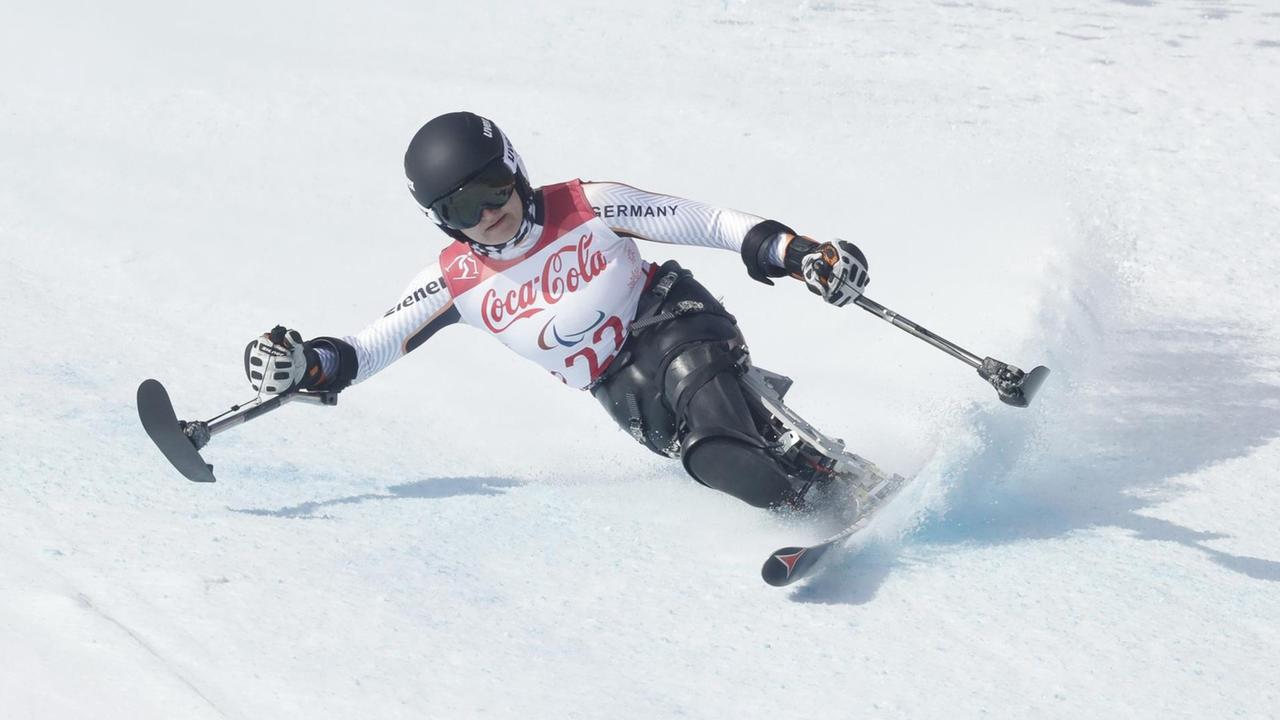 Forster liegt auf dem weißen Schnee in der Kurve. In den Händen hält sie kurze Stöcke mit Laufflächen.