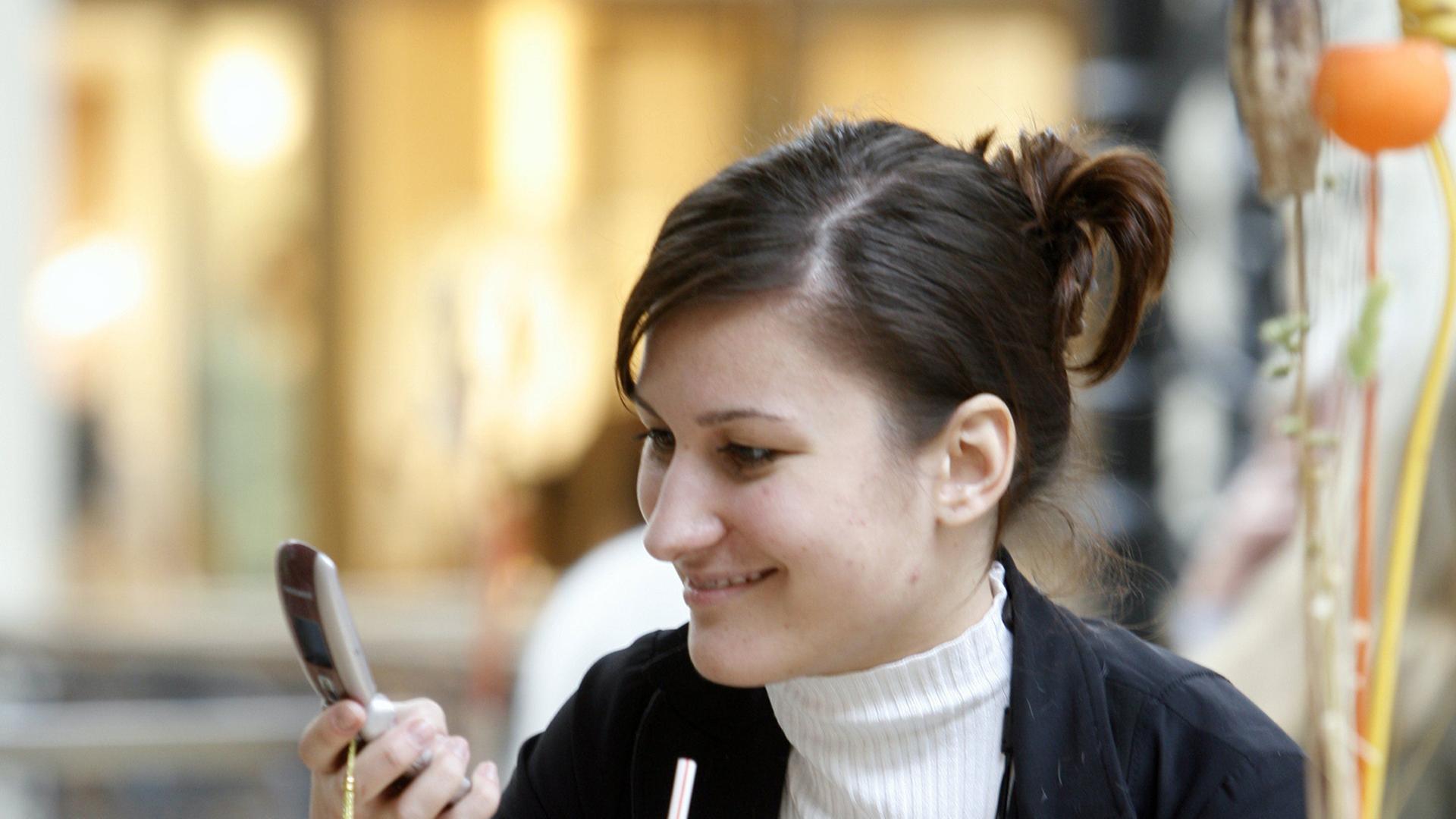 Eine junge Frau schaut auf ihr Mobiltelefon, während sie in einem Cafe sitzt. 