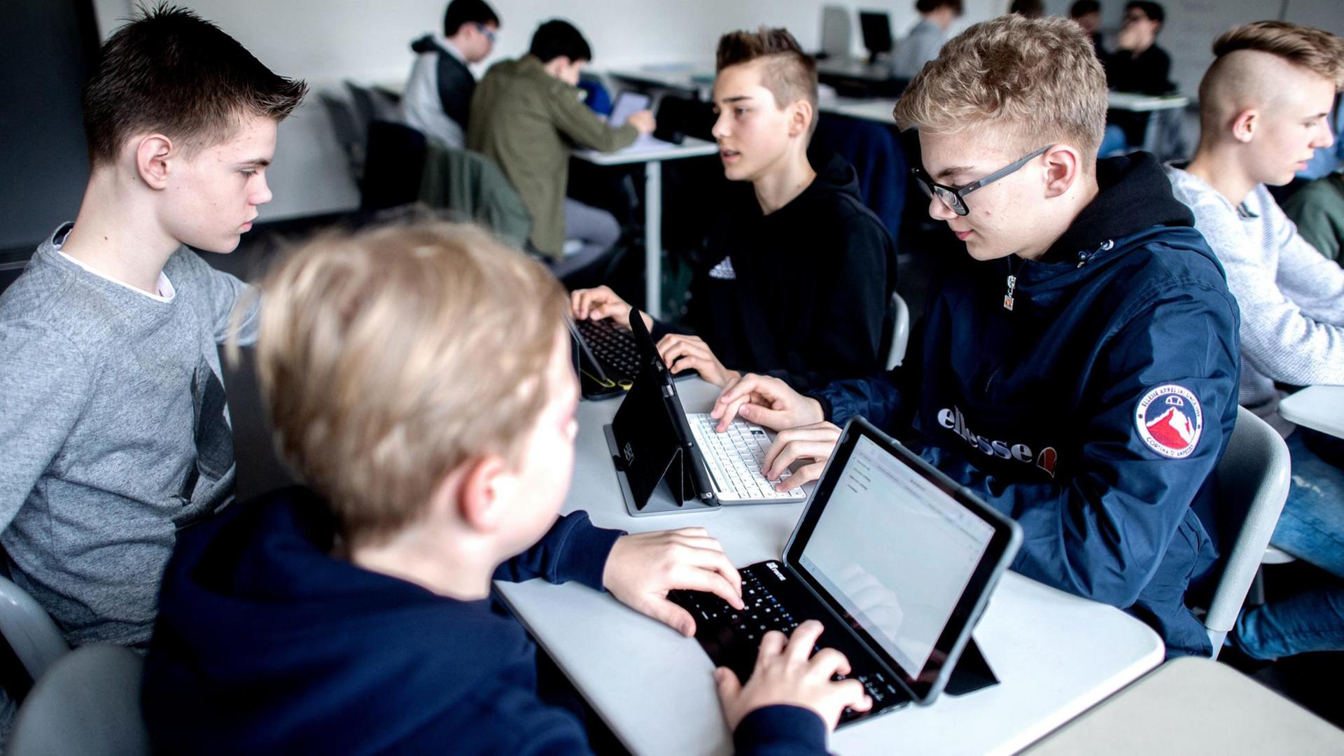 Schüler sitzen in einem Klassenzimmer und lernen mit Laptops.