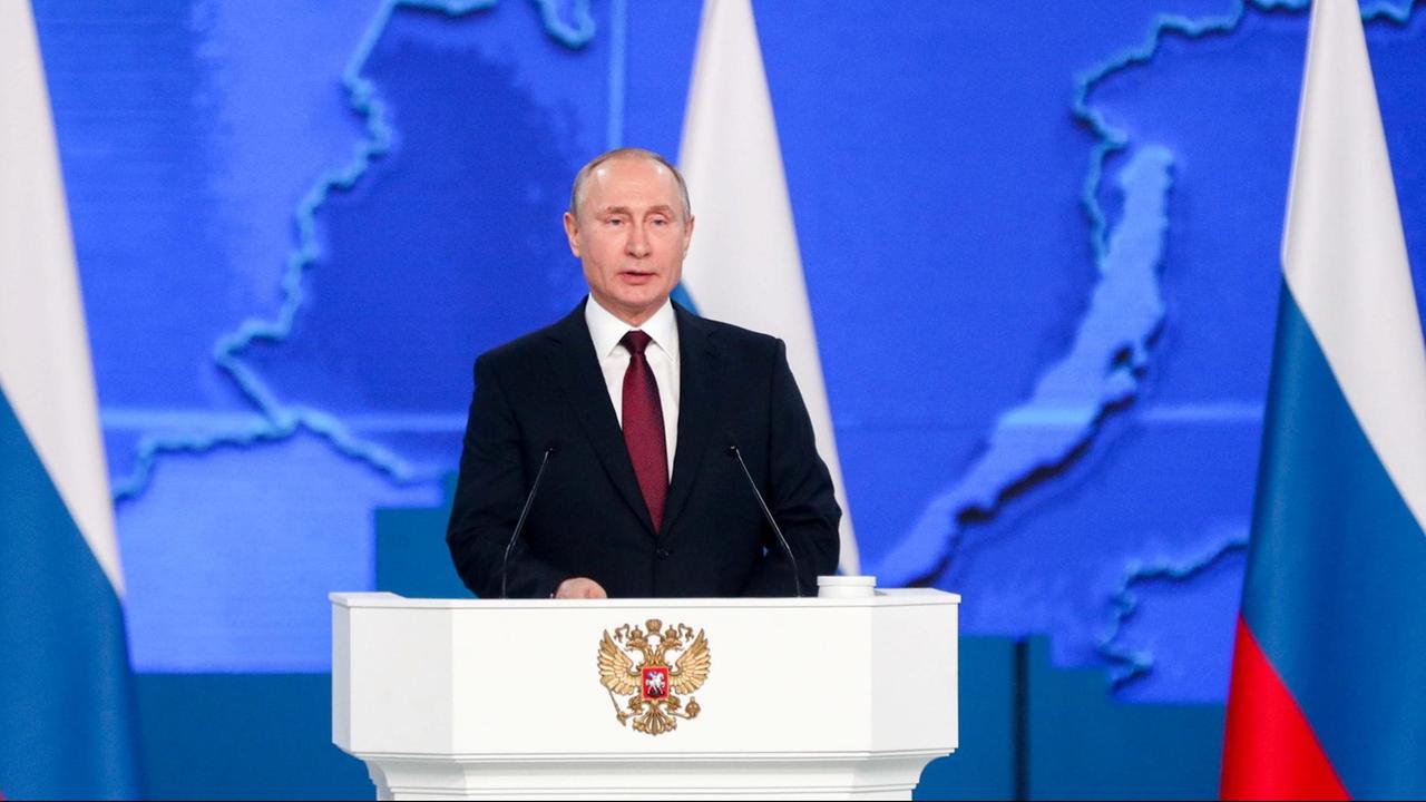 Der russische Präsident Putin steht an einem Rednerpult und spricht. Im Hintergrund sind mehrere russische Flaggen zu sehen.