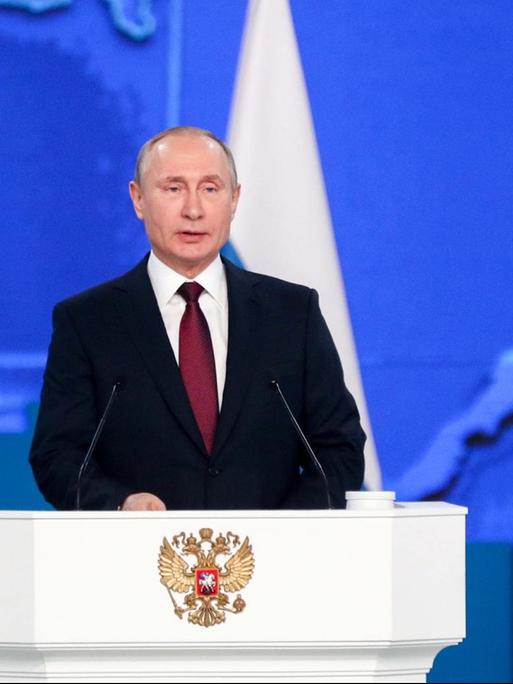 Der russische Präsident Putin steht an einem Rednerpult und spricht. Im Hintergrund sind mehrere russische Flaggen zu sehen.