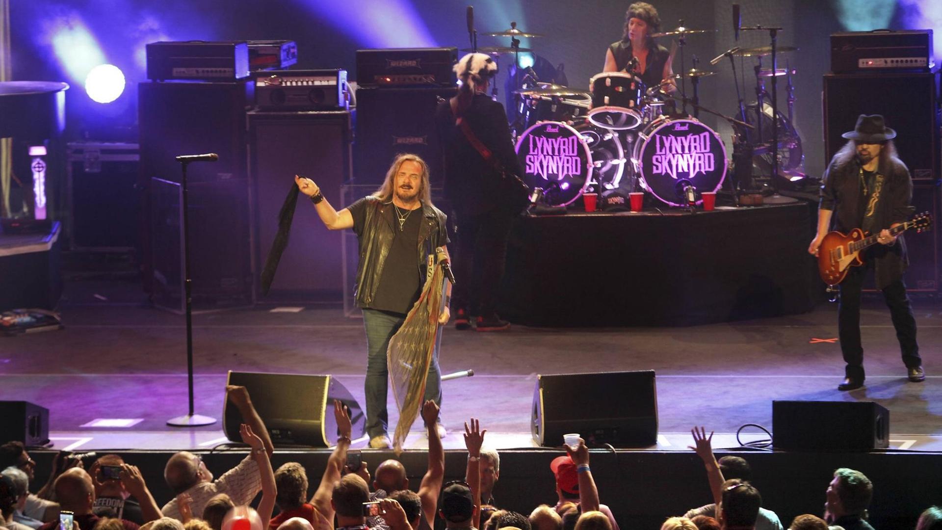 Das Bild zeigt die US-Rockband Lynyrd Skynyrd mit Sänger Johnny Van Zant am Mikrophon auf einer Bühne, davor Fans.