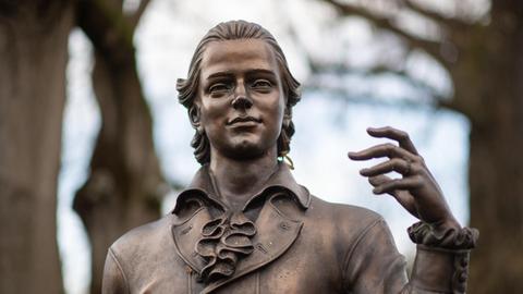 Eine Skulptur des Künstlers Waldemar Schröder, die Friedrich Hölderlin darstellt, steht vor Bäumen.