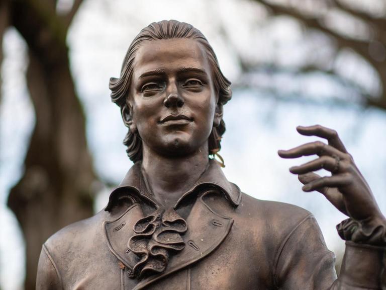 Eine Skulptur des Künstlers Waldemar Schröder, die Friedrich Hölderlin darstellt, steht vor Bäumen.