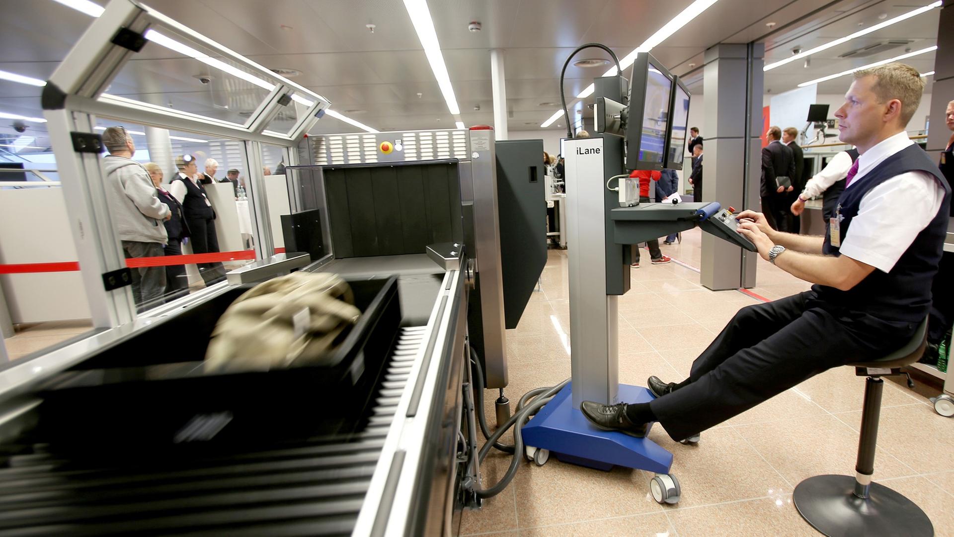 Ein Sicherheitsbeamter eines Flughafens sitzt an Kontrollmonitoren bei der Handgepäckkontrolle.