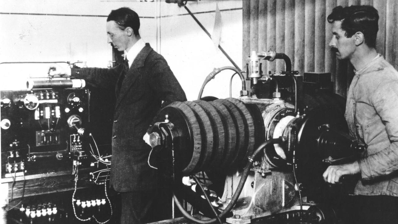 Auf einer historischen Fotografie sind zwei Männer zu sehen, die an technischen Geräten beschäftigt sind.