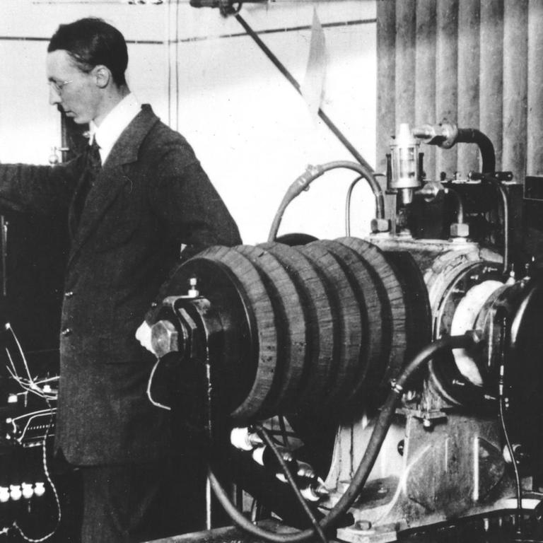 Auf einer historischen Fotografie sind zwei Männer zu sehen, die an technischen Geräten beschäftigt sind.
