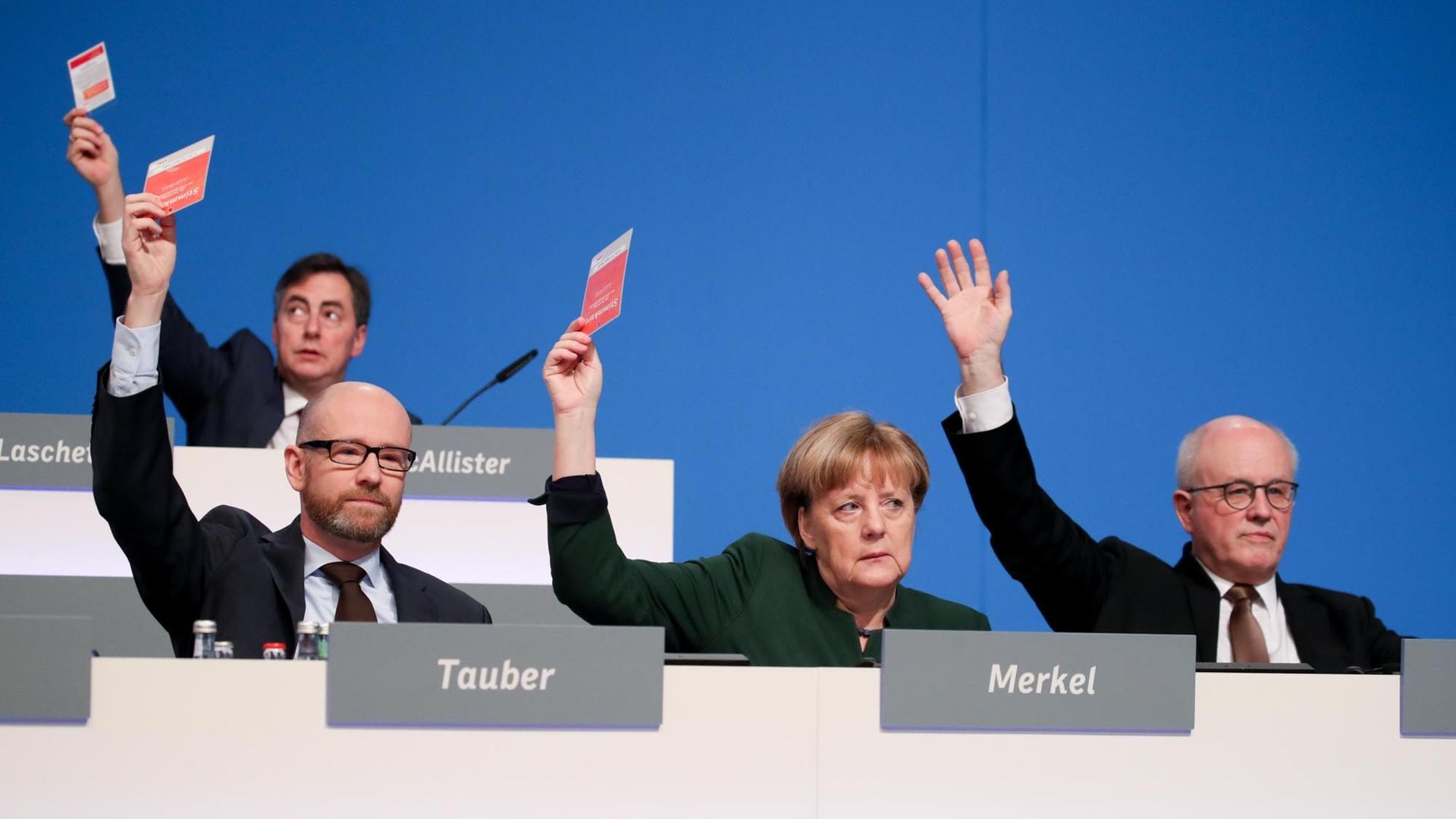 Bundeskanzlerin Angela Merkel (CDU) hält am 07.12.2016 beim 29. Bundesparteitag der CDU in Essen (Nordrhein-Westfalen) neben CDU-Generalsekretär Peter Tauber (l) und Unionsfraktionschef Volker Kauder (CDU) die Stimmkarte hoch.