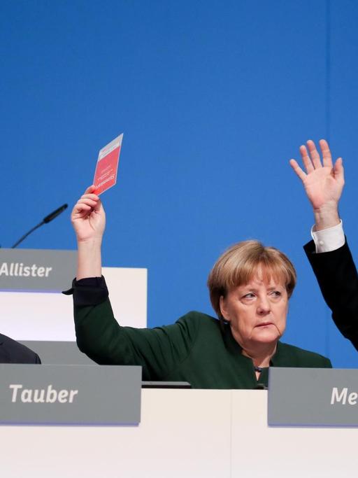 Bundeskanzlerin Angela Merkel (CDU) hält am 07.12.2016 beim 29. Bundesparteitag der CDU in Essen (Nordrhein-Westfalen) neben CDU-Generalsekretär Peter Tauber (l) und Unionsfraktionschef Volker Kauder (CDU) die Stimmkarte hoch.