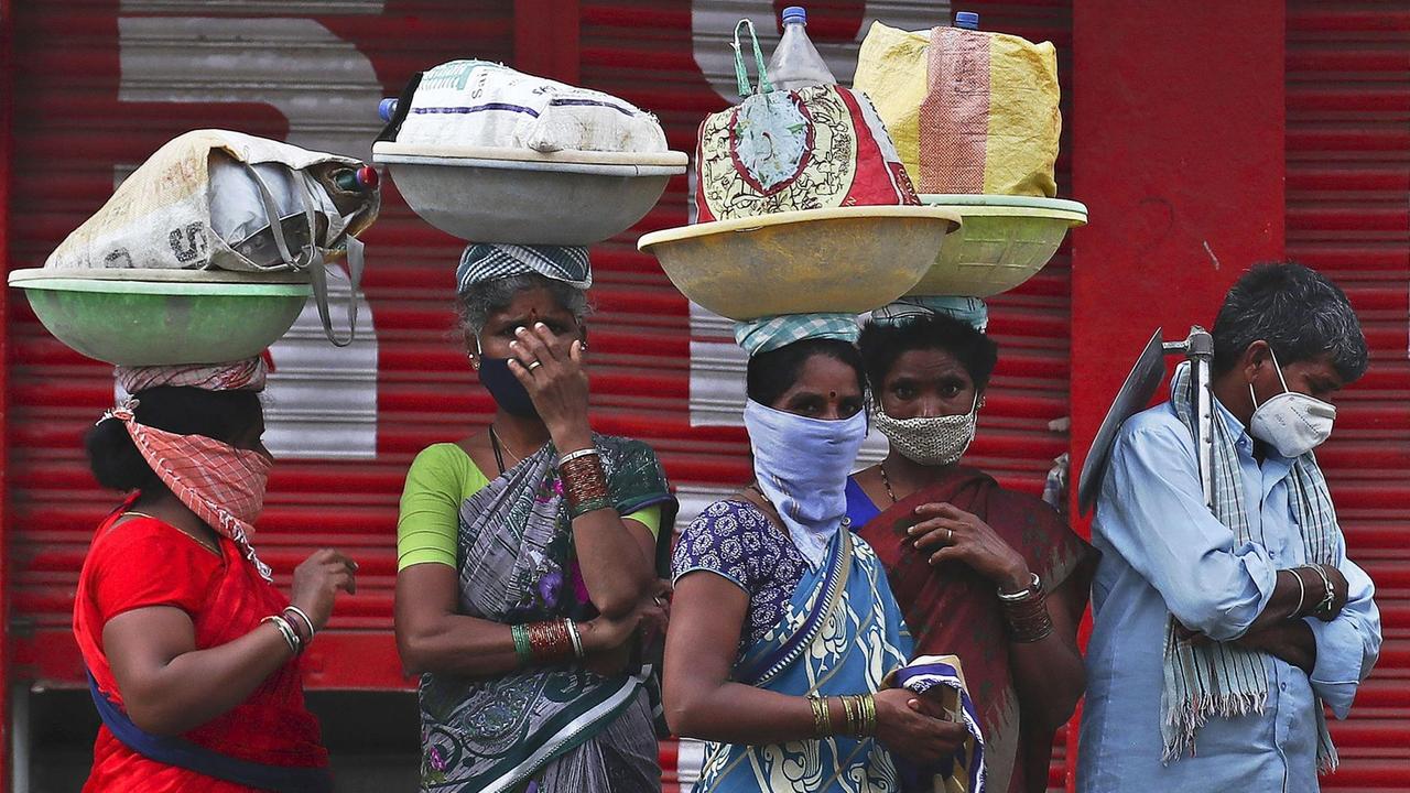 Indien, Hyderabad: Tagelöhnerinnen warten während des coronabedingten Lockdowns auf einem Gehweg auf eine Transportmöglichkeit.