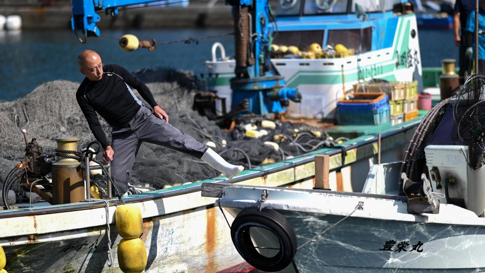 Ein japanischer Fischer arbeitet auf seinem Boot an einem Pier, im Hintergrund liegen Fischernetze.