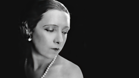 Die brasilianische Pianistin Magda Tagliaferro lebte viele Jahre in Paris und setzte sich für das französische und spanische Musik-Repertoire ein. Schwarz-weiß-Fotografie im Halb-Profil. Sie trägt Perlenohrringe und eine Perlenkette, das schwarze Kleid ist auf der linken Seite schulterfrei.