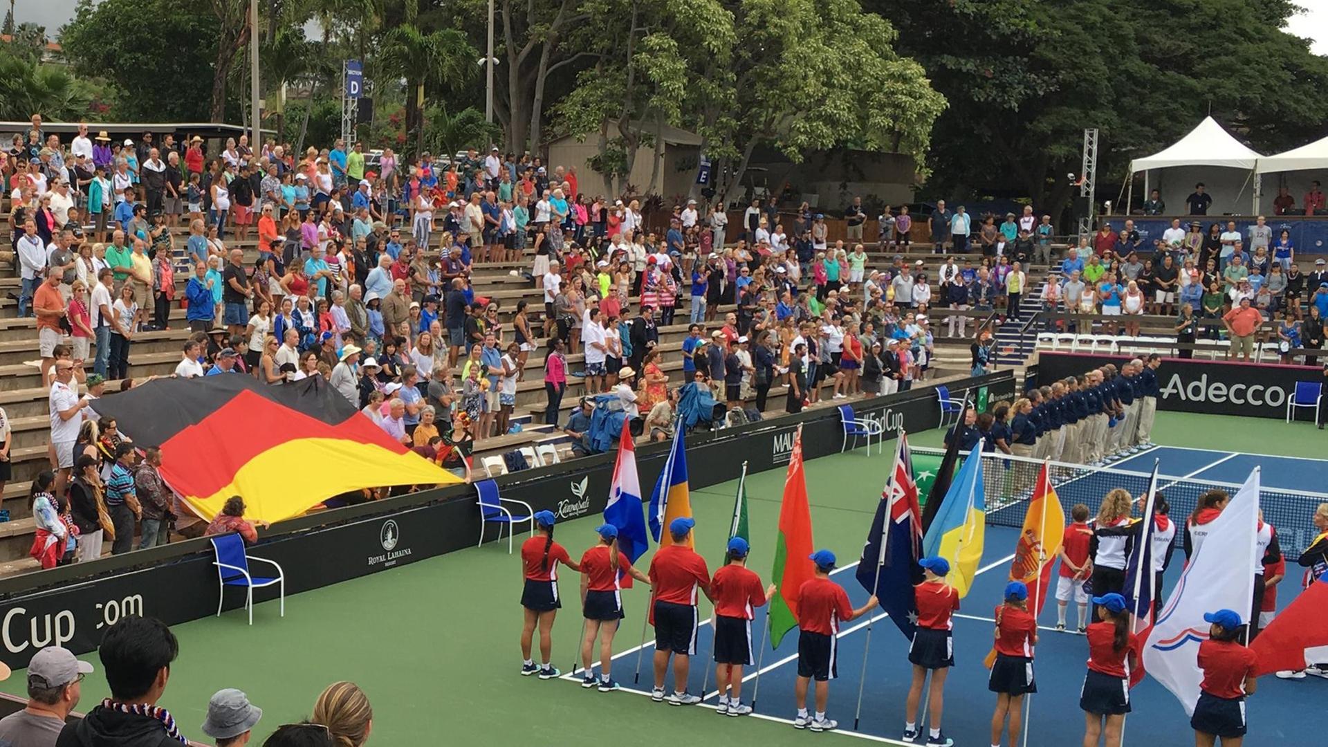 Blick auf den Center Court mit einer ausgebreiteten Deutschlandflagge auf der kleinen Tribüne, auf dem Platz stehen die Akteure zum Absingen der Nationalhymne bereit.