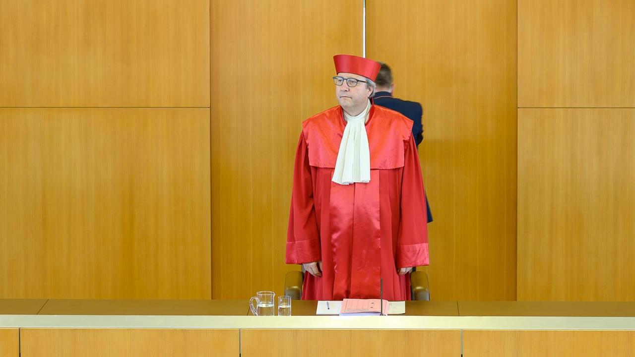 Der Richter trägt einen roten Umhang und steht vorne im Gerichts-Saal an seinem Platz.