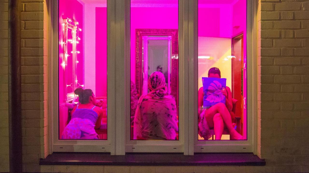 Ein im pinken Licht erleuchtetes Fenster mit drei Silhouetten von Frauen im Rotlichtviertel von Oberhausen