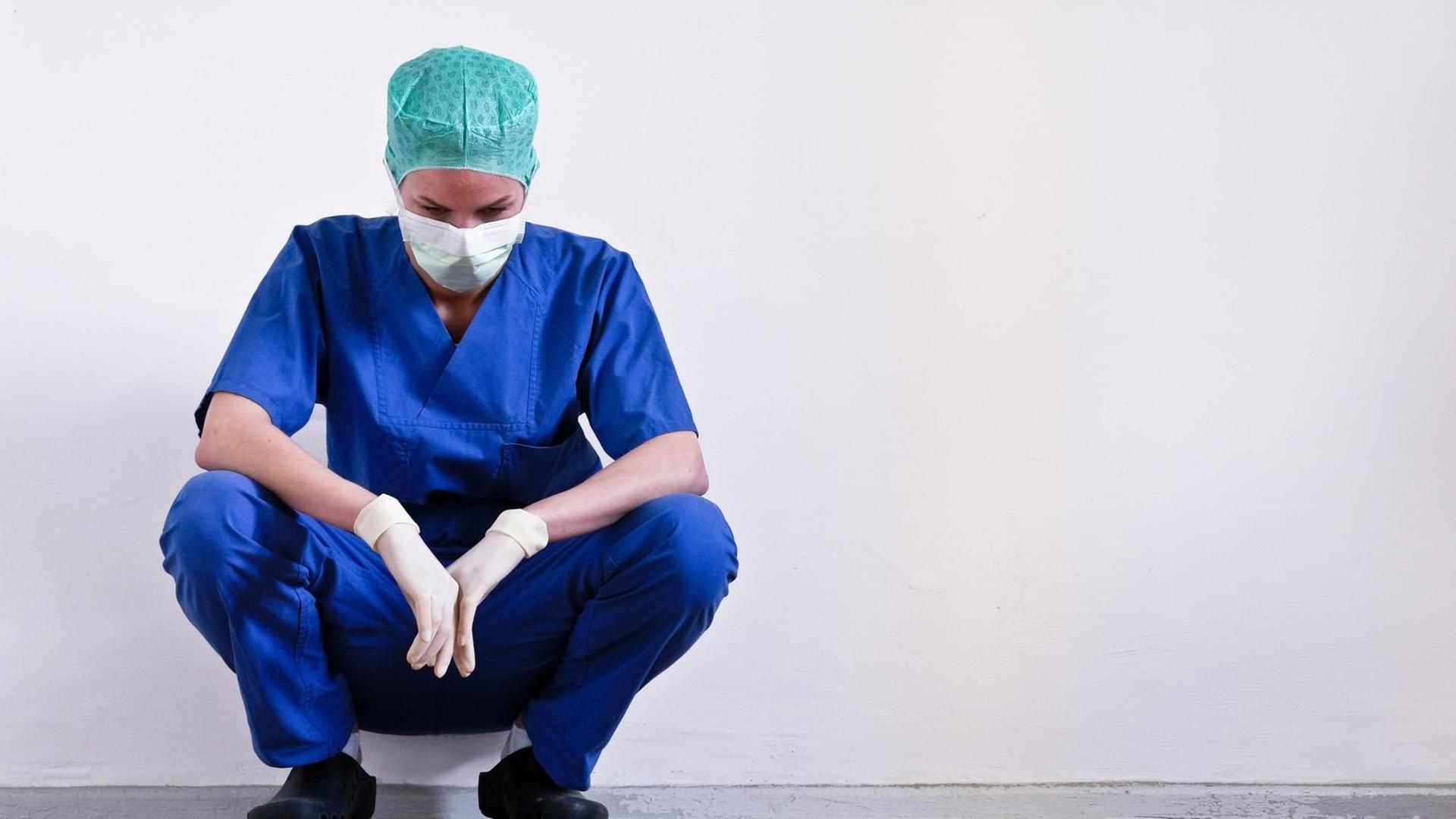 Eine erschöpfte Ärztin hockt noch in OP-Kleidung nach einer Operation am Boden.