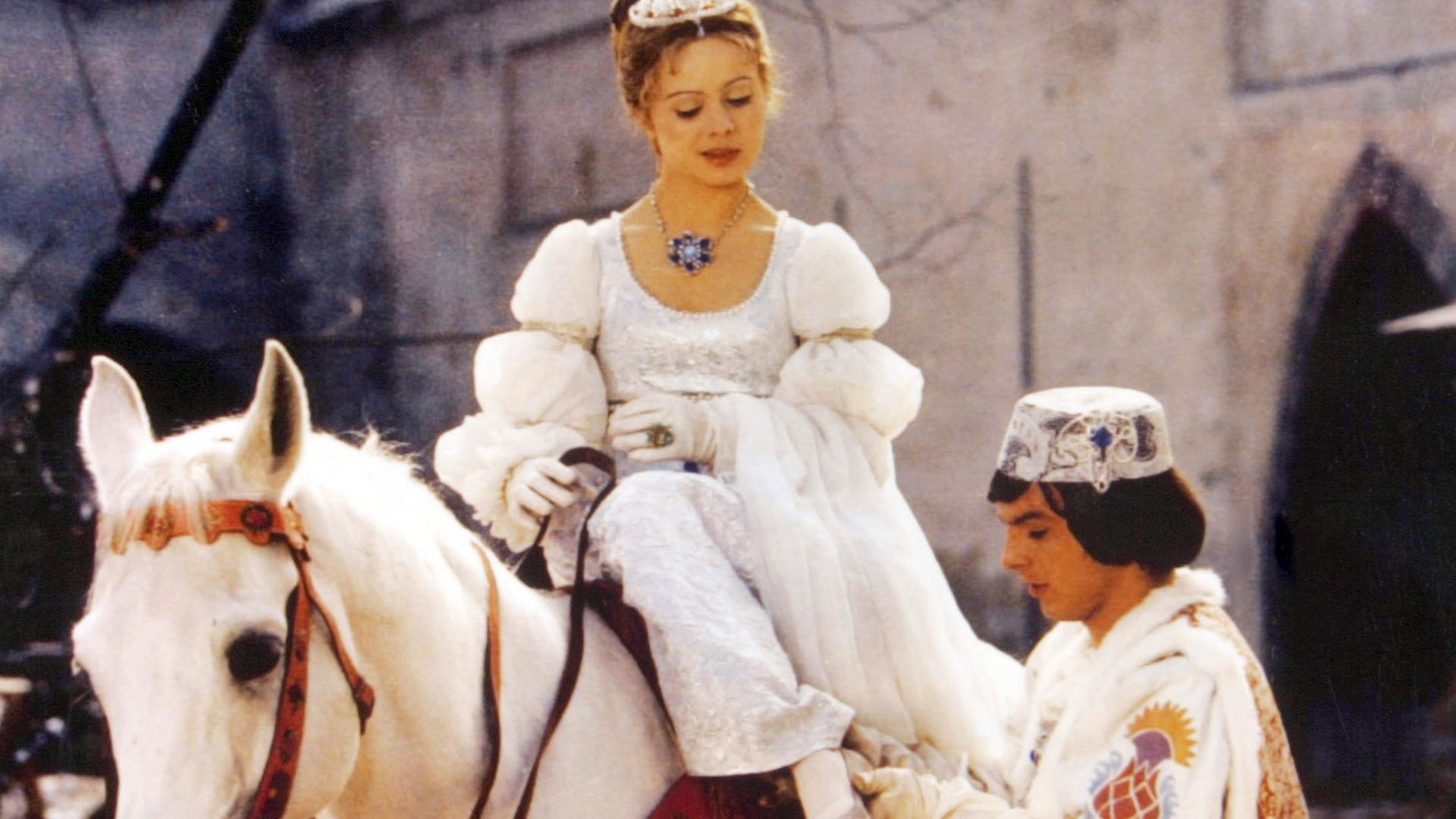 Szene aus dem Film "Drei Haselnüsse für Aschenbrödel": Der Prinz passt Aschenbrödel den verlorenen Schuh an. Sie sitzt dabei auf einem weißen Pferd und blickt zu ihm hinunter.