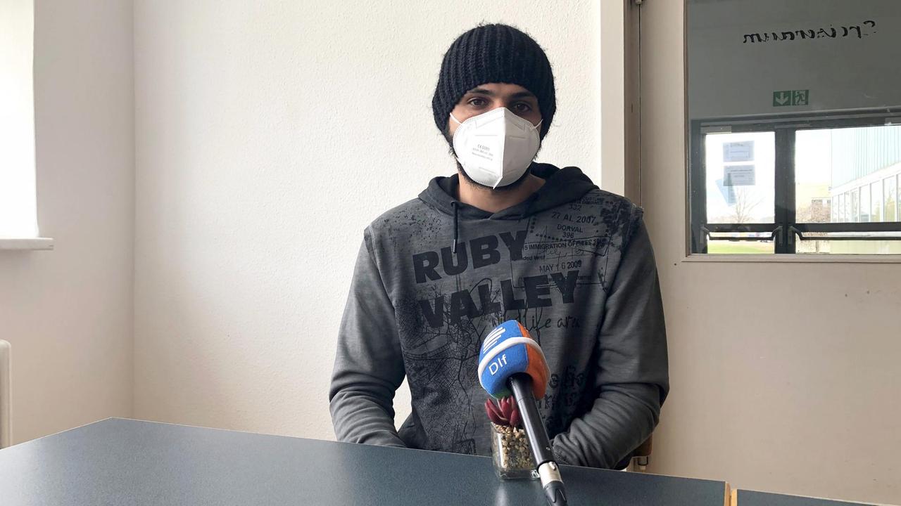 Ahmed Alabd sitzt in einem Raum. Er trägt Wollmütze und wegen der Corona-Pandemie eine Maske über Mund und Nase.