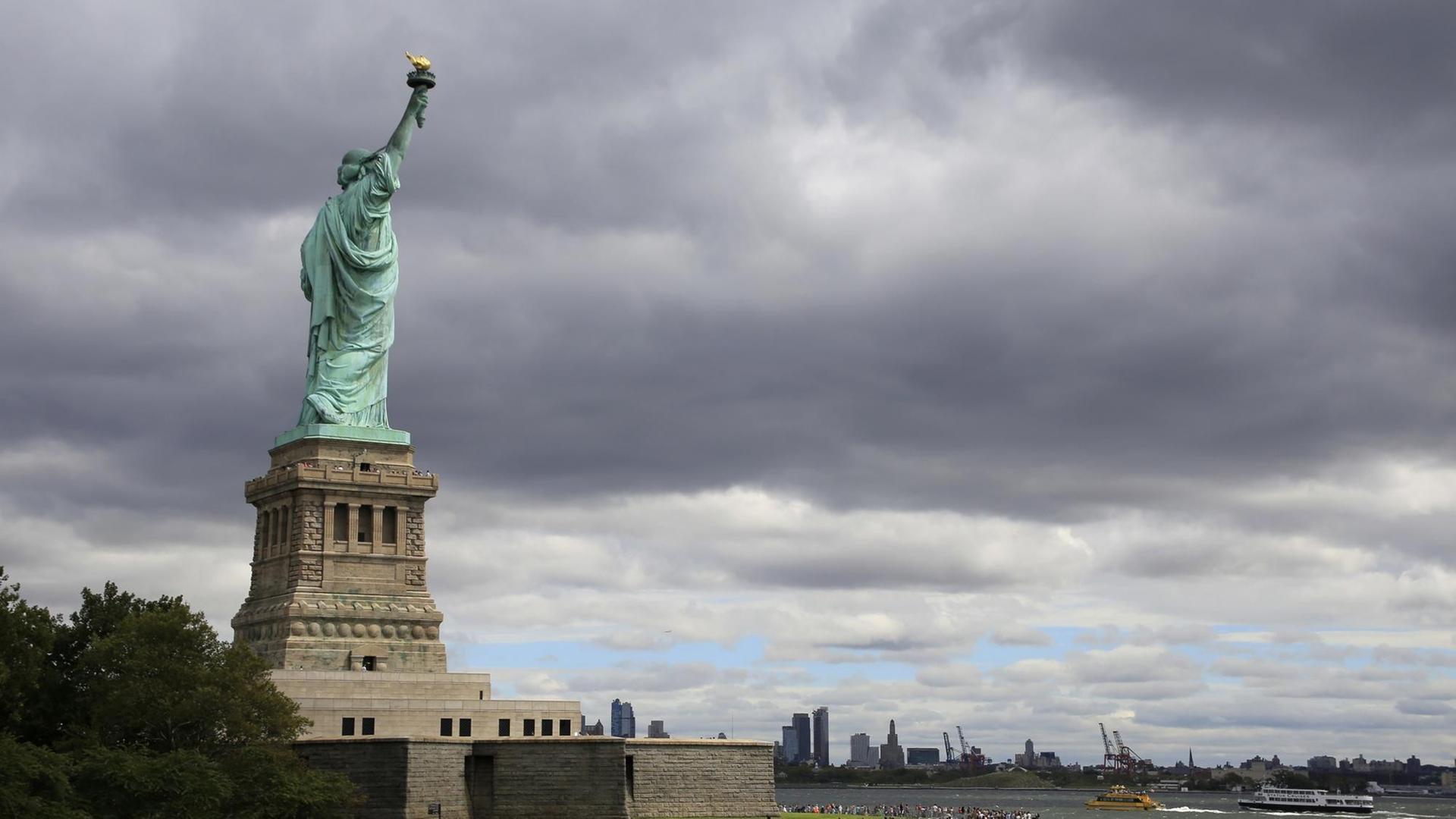 Die Freiheitsstatue auf Liberty Island auf ihrem Sockel, im Hintergrund angedeutet die Skyline von New York