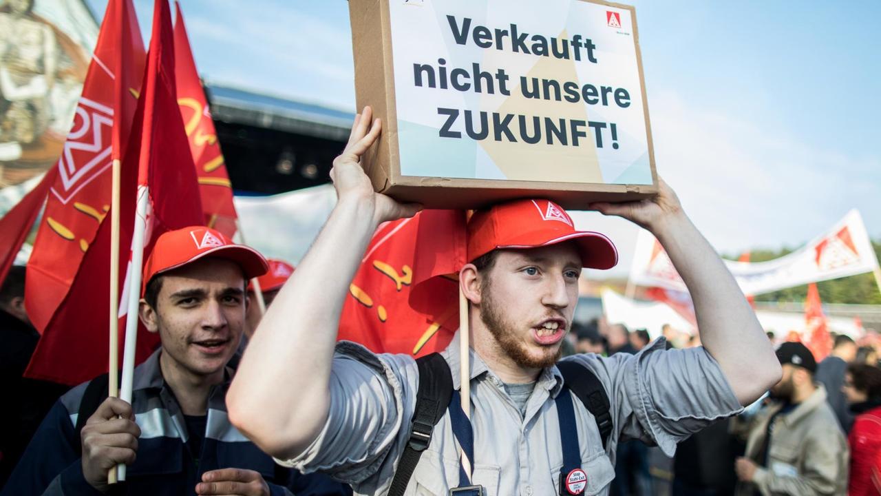 Ein Mitarbeiter in Arbeitskleidung hält ein Schild mit der Aufschrift "Verkauft nicht unsere Zukunft" über den Kopf. 