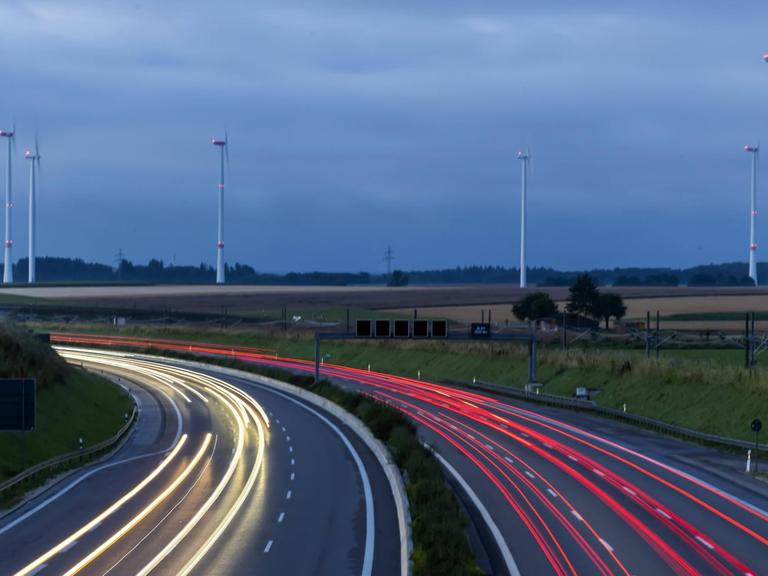 Autobahn A8 am frühen Morgen mit Lichtspuren der Autos. Im Hintergrund ein Windpark.