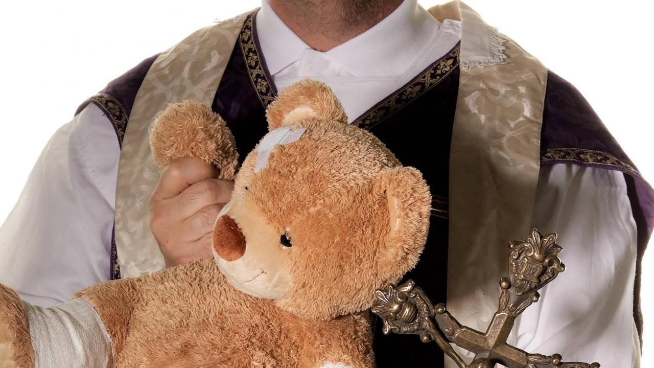 Ein Priester mit einem Teddybären, der Verbände einem Arm und einem Bein trägt