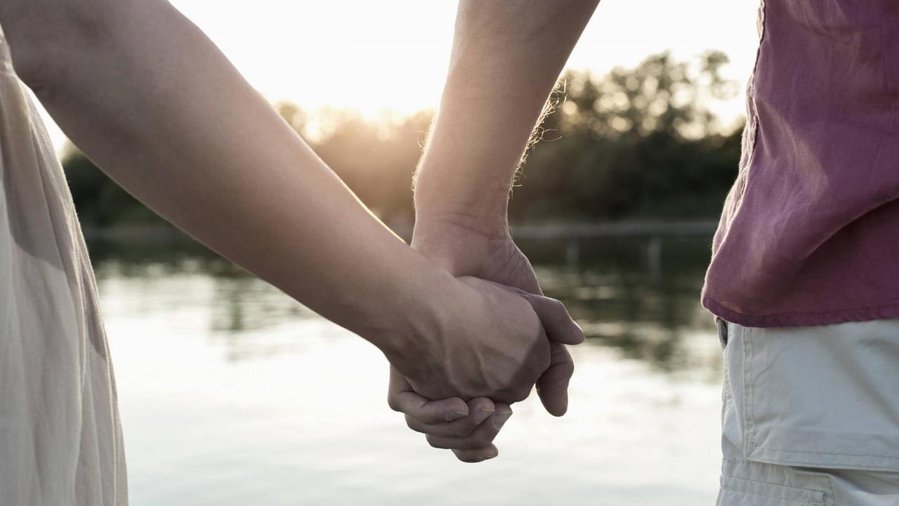 Ein Paar hält Händchen vor einem See, während die Sonne untergeht.