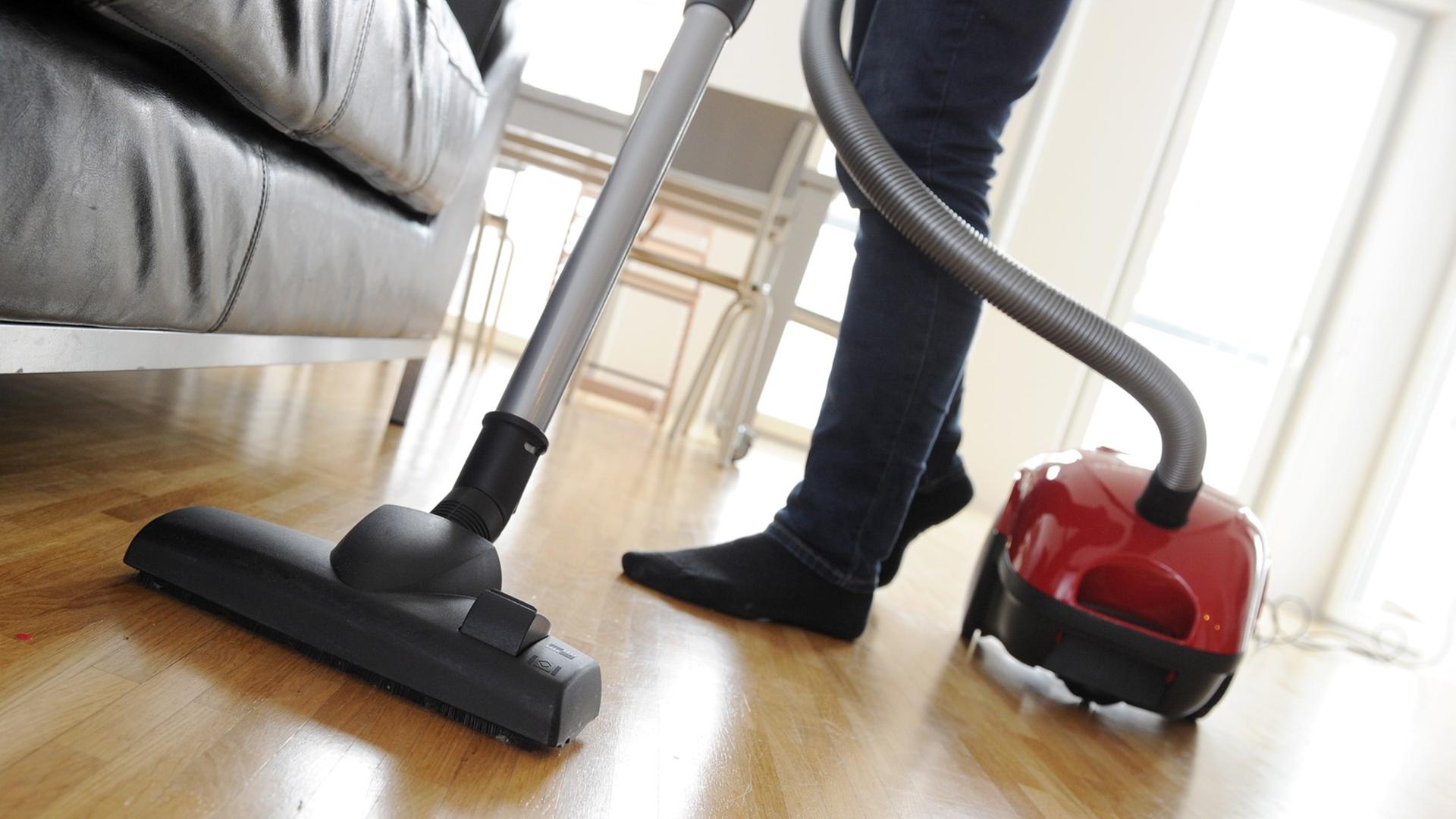 Eine Frau saugt mit einem Staubsauger den Fußboden eines Wohnzimmers.
