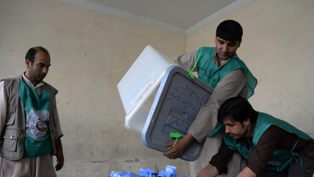Männer schütten eine Box mit Wahlzetteln aus.