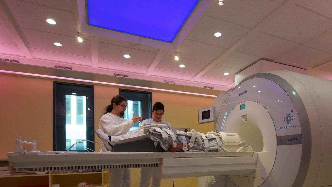 Ein MRT-Scanner in einem Universitätsklinikum: Ein Patient liegt zur Untersuchung bereit, während zwei Ärzte neben diesem stehen. 