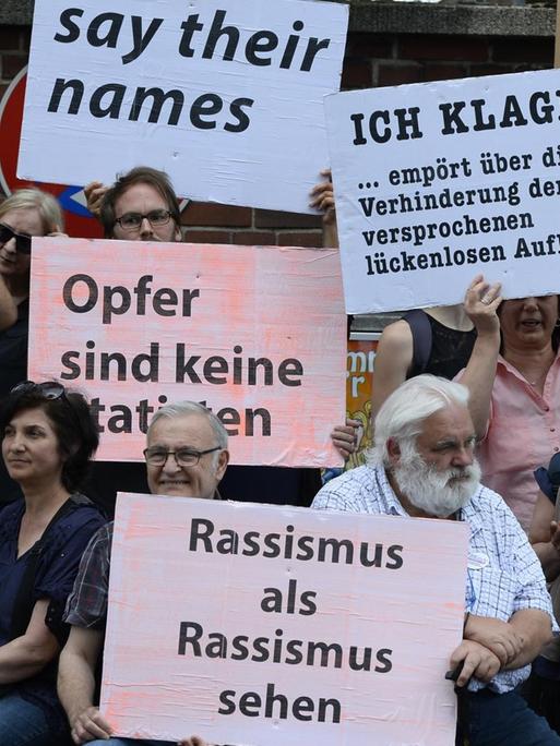 Teilnehmer einer Schweigeminute erinnern mit Plakaten auf der Kölner Keupstrasse am 15. Jahrestag an den NSU-Nagelbombenanschlag
