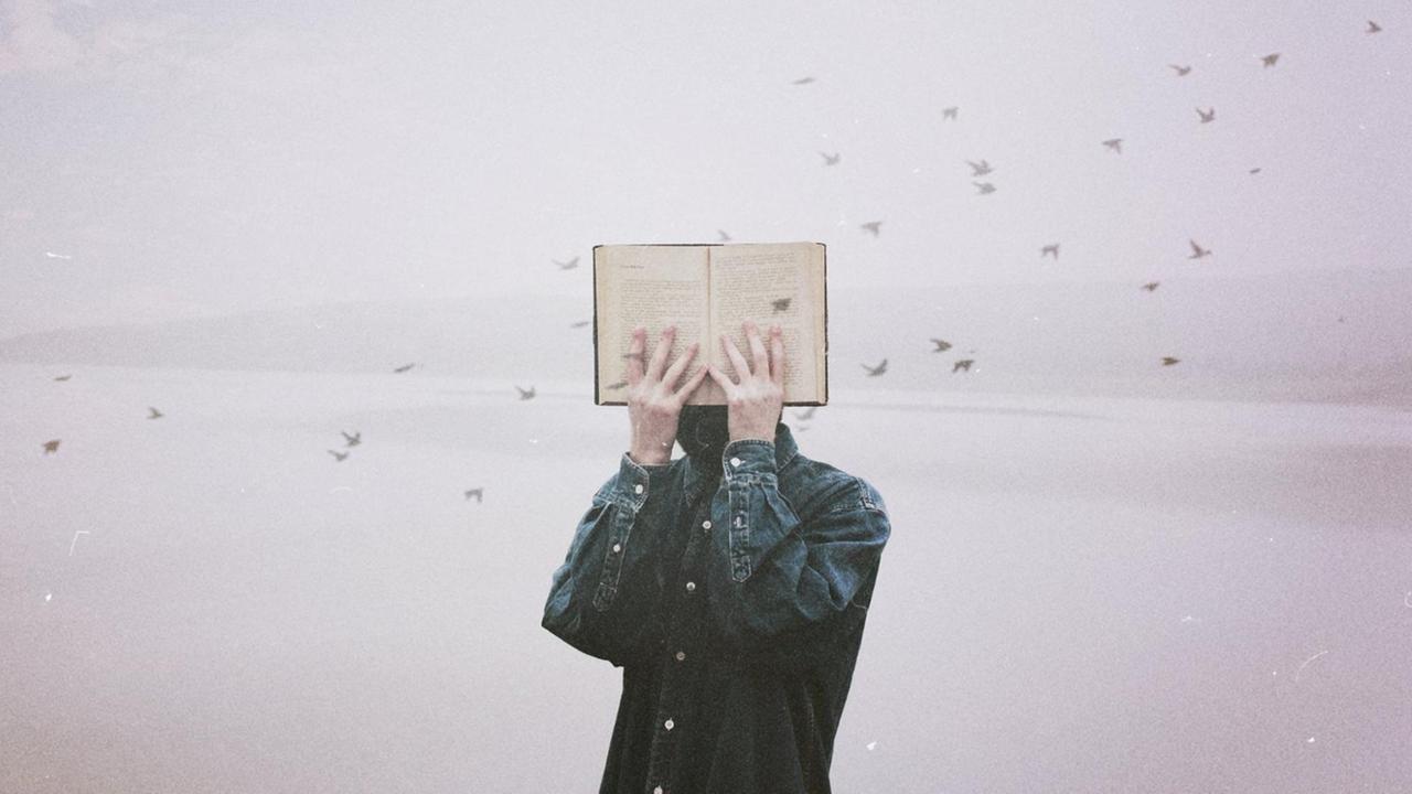 Ein Mann hält sich ein Buch vor sein Gesicht, im Hintergrund fliegt ein Schwarm kleiner Vögel durch das Bild.